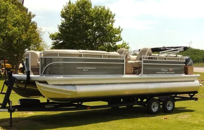 Slide: The Image of 2024 Sun Tracker Party Barge 24 DLX pontoon boat on trailer, parked on grass. - 4