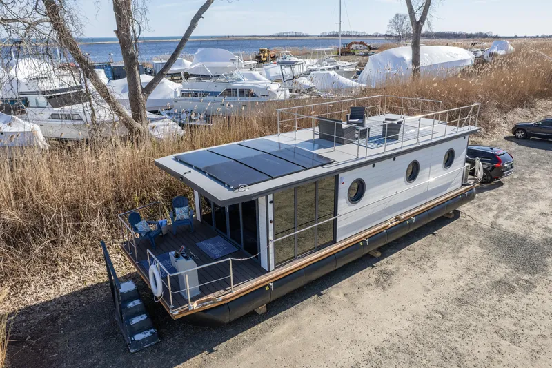 Slide: The Image of 2024 Waterlodge Apart EL houseboat docked near a marina with solar panels on the roof. - 2