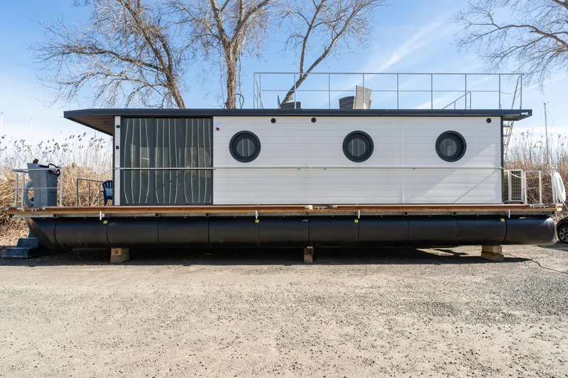 Slide: The Image of 2024 Waterlodge Apart EL houseboat with circular windows and rooftop deck, docked on land. - 28