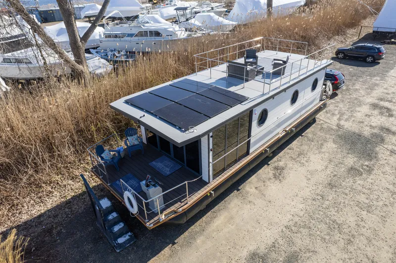 Slide: The Image of Waterlodge Apart EL 2024 houseboat with rooftop solar panels and outdoor seating, docked near other boats. - 33