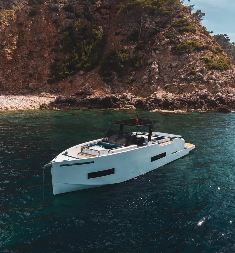Slide: The Image of 2024 De Antonio Yachts D50 OPEN in serene coastal waters near rocky cliffs. - 1