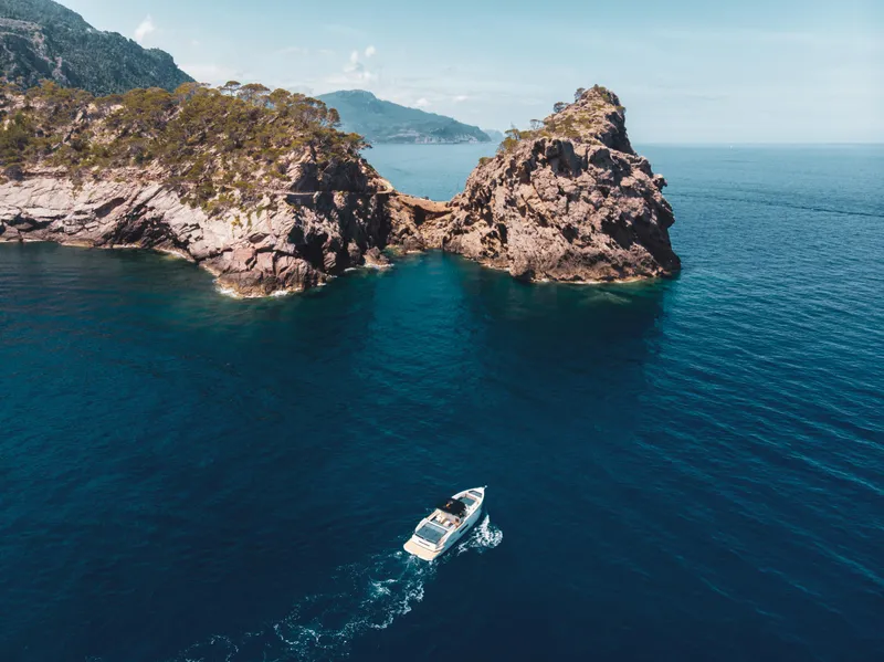 Slide: The Image of 2024 De Antonio Yachts D50 OPEN cruising near rocky coastline in clear blue waters. - 5
