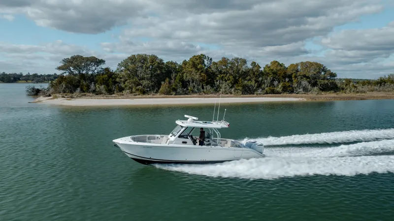 Slide: The Image of 2022 Pursuit S 328 boat cruising on a serene lake with a forested shoreline. - 11