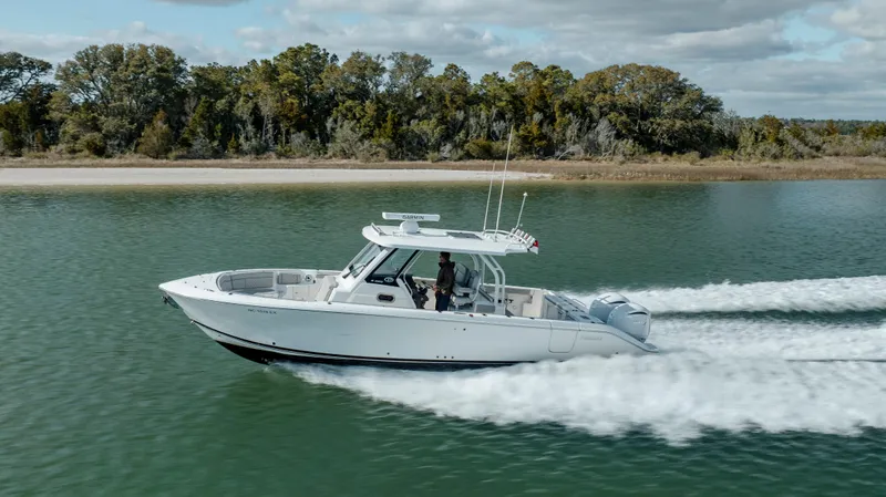 Slide: The Image of 2022 Pursuit S 328 boat cruising on a serene lake with a forested shoreline. - 12