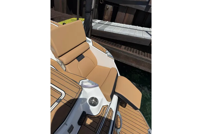 Slide: The Image of 2024 MasterCraft X26 boat with tan seating and cup holder, docked by the water. - 16