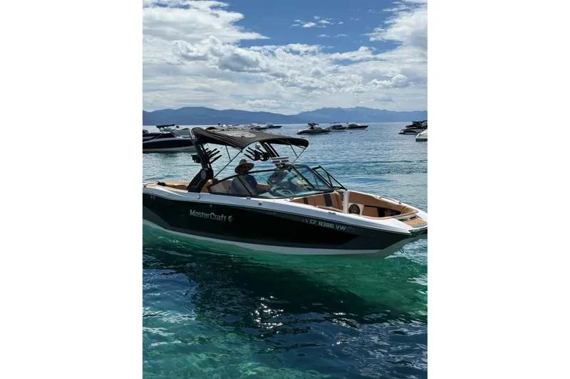 Slide: The Image of 2024 MasterCraft X26 boat cruising on clear blue water under a partly cloudy sky. - 2