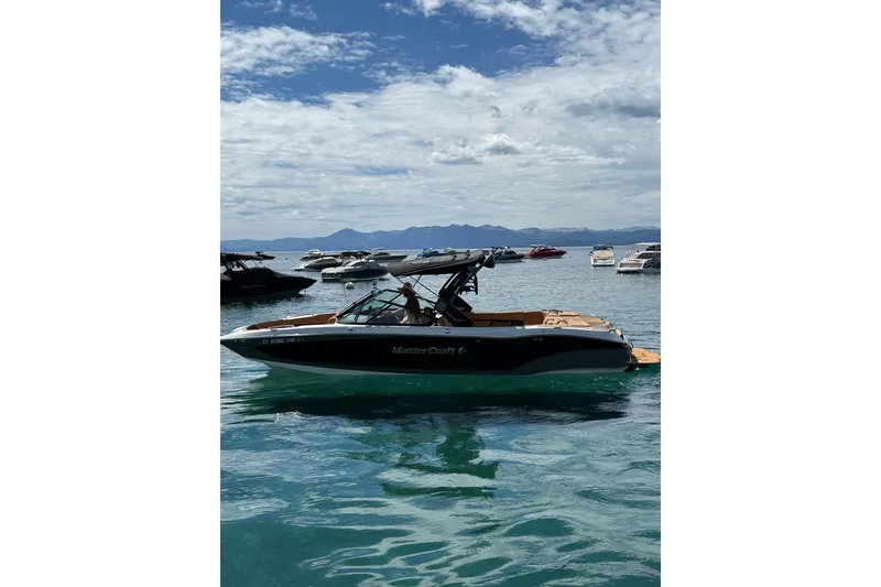 Slide: The Image of 2024 MasterCraft X26 boat on a serene lake with other boats in the background. - 3