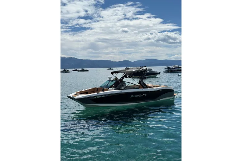 Slide: The Image of 2024 MasterCraft X26 boat on clear blue water under a partly cloudy sky. - 1