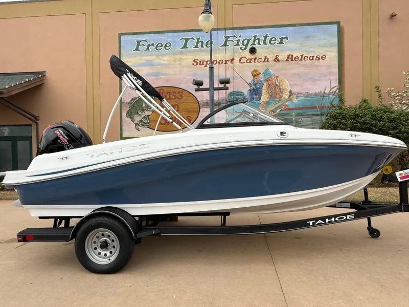 Slide: The Image of 2023 Tahoe 185 S boat on trailer, blue and white, parked near fishing mural. - 2