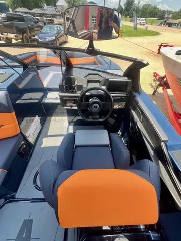 Slide: The Image of 2024 Axis Wake Research A225 boat interior with orange and blue seating, steering wheel, and dashboard. - 10