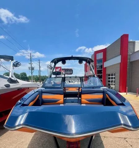 Slide: The Image of 2024 Axis Wake Research A225 boat with blue and orange seating, displayed outdoors. - 5