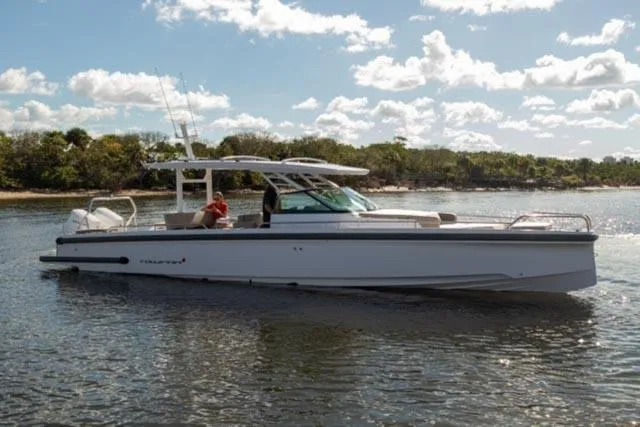 Slide: The Image of 2024 Axopar 37 Sun Top boat on calm water, sunny day, lush shoreline. - 0