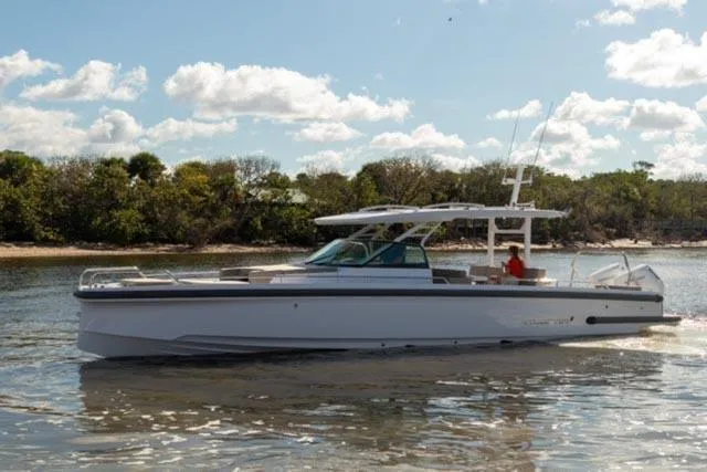 Slide: The Image of 2024 Axopar 37 Sun Top boat cruising on a sunny day near a forested shoreline. - 8