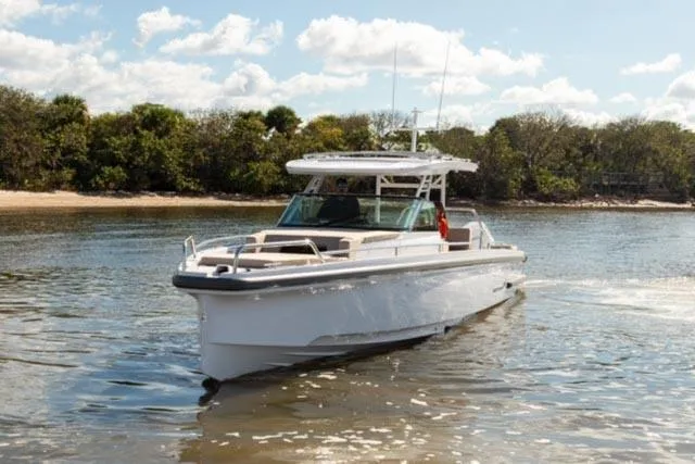 Slide: The Image of 2024 Axopar 37 Sun Top boat cruising on a sunny day near a forested shoreline. - 9