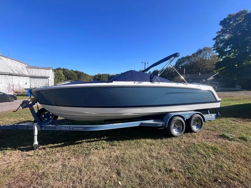 Slide: The Image of 2024 Cobalt CS23 boat on trailer, parked on grass under clear blue sky. - 1