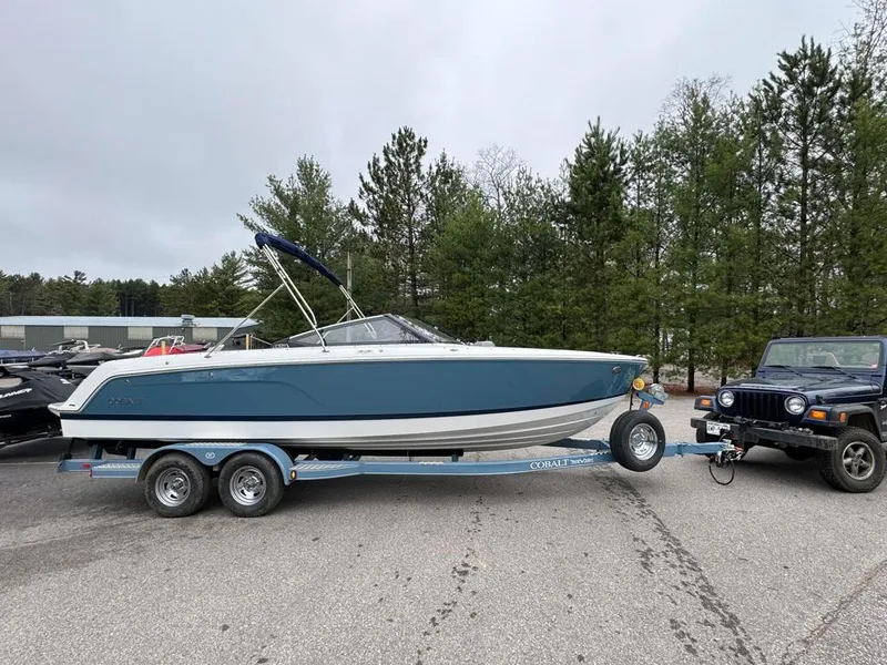 Slide: The Image of 2024 Cobalt CS23 boat on trailer, parked near trees and a Jeep. - 10