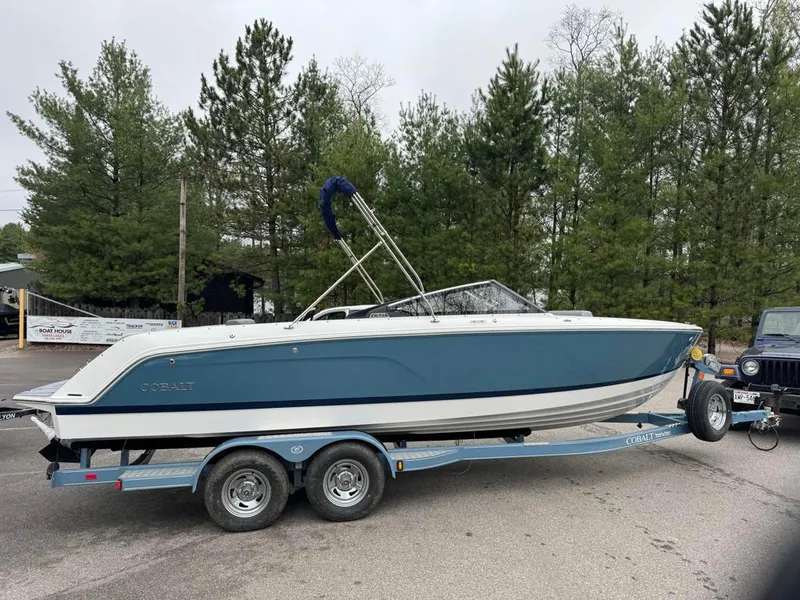 Slide: The Image of 2024 Cobalt CS23 boat on trailer, parked outdoors near trees. - 12