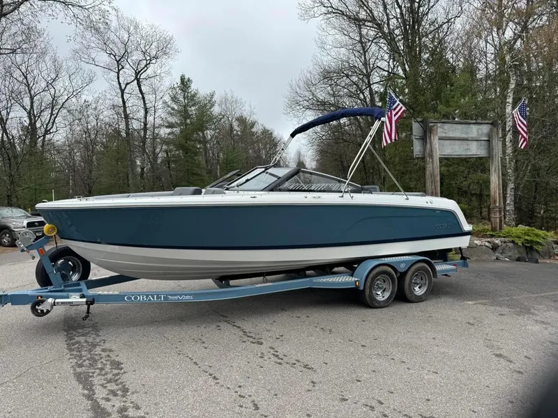 Slide: The Image of 2024 Cobalt CS23 boat on trailer, parked outdoors with trees and flags in the background. - 3