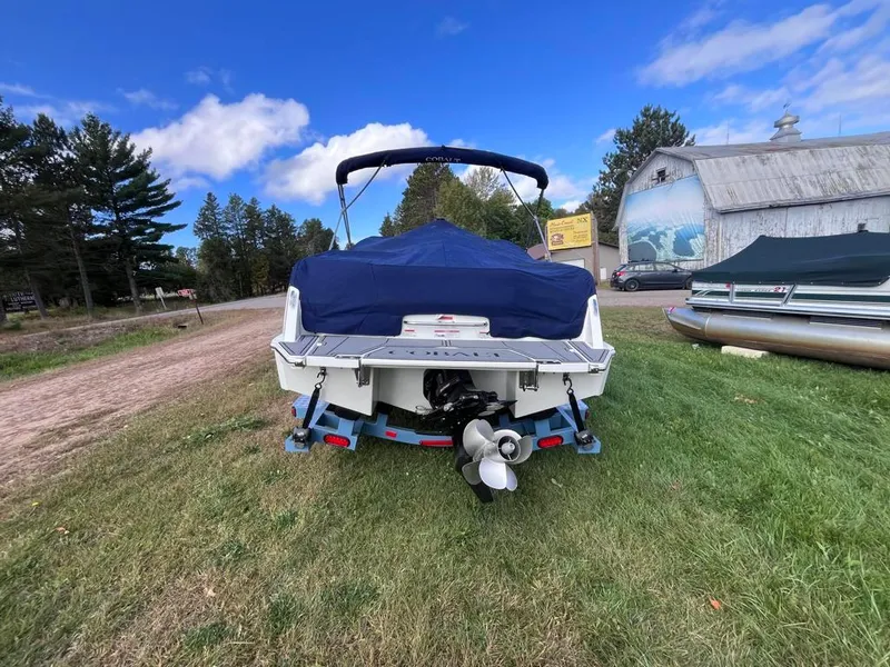 Slide: The Image of 2024 Cobalt CS23 boat with blue cover, parked on grass near rustic barn. - 7