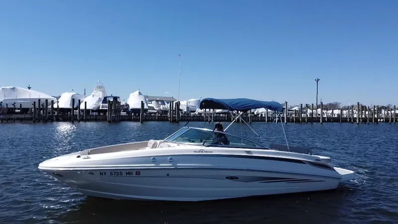 The Image of 2011 Sea Ray 240 Sundeck boat on water near marina with blue sky. - 0