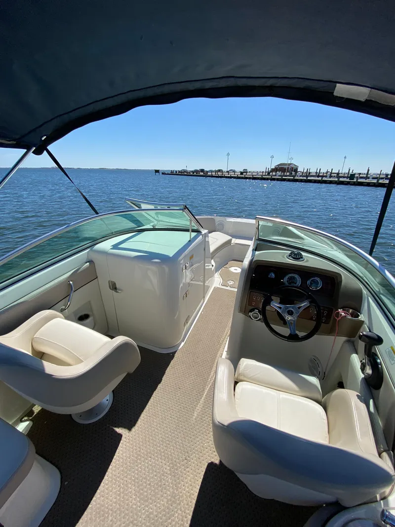 Slide: The Image of 2011 Sea Ray 240 Sundeck boat interior with steering wheel and seating, on calm water. - 11