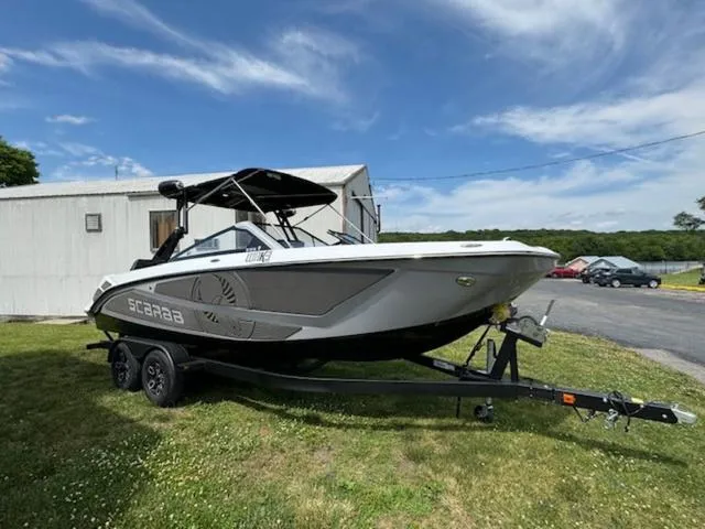 Slide: The Image of 2025 Scarab 235 Wake boat on trailer, parked on grass near a building. - 3
