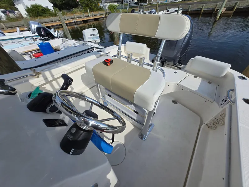 Slide: The Image of 2021 Bulls Bay 200 CC boat interior with steering wheel and seating, docked by the water. - 28