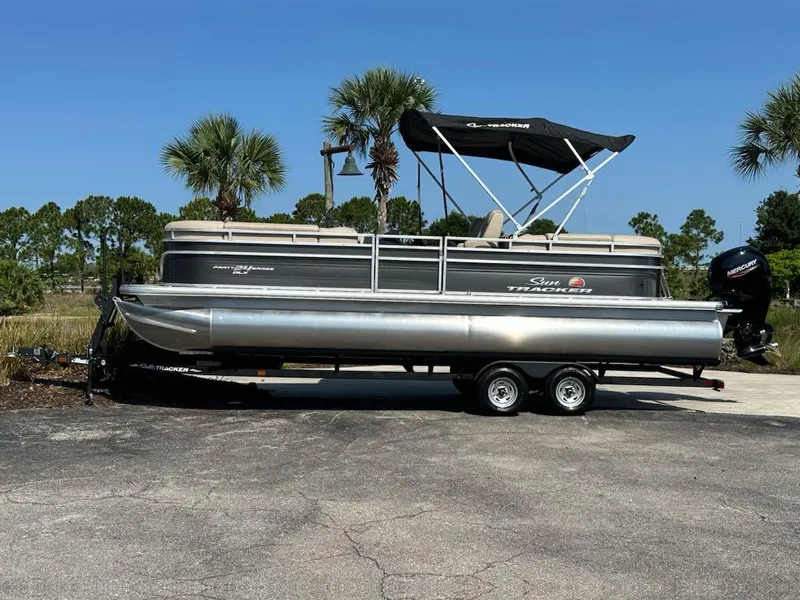 The Image of 2024 Sun Tracker Party Barge 24 DLX pontoon boat on a trailer, parked outdoors. - 0