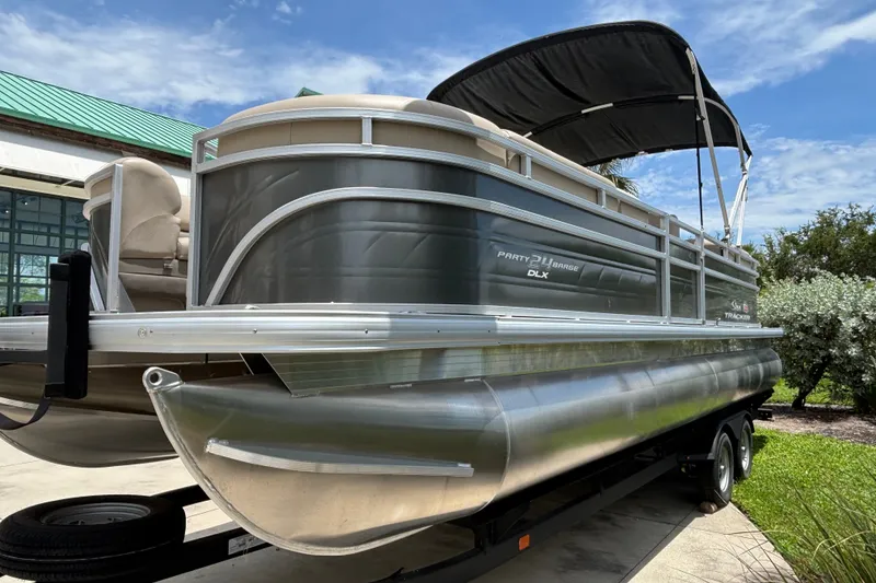 The Image of 2024 Sun Tracker Party Barge 24 DLX pontoon boat with canopy, parked on a trailer. - 0