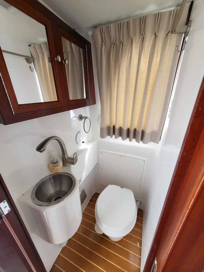 Slide: The Image of Compact bathroom in a 2012 Crusader Boats outboard cruiser, featuring sink, toilet, and wooden flooring. - 30