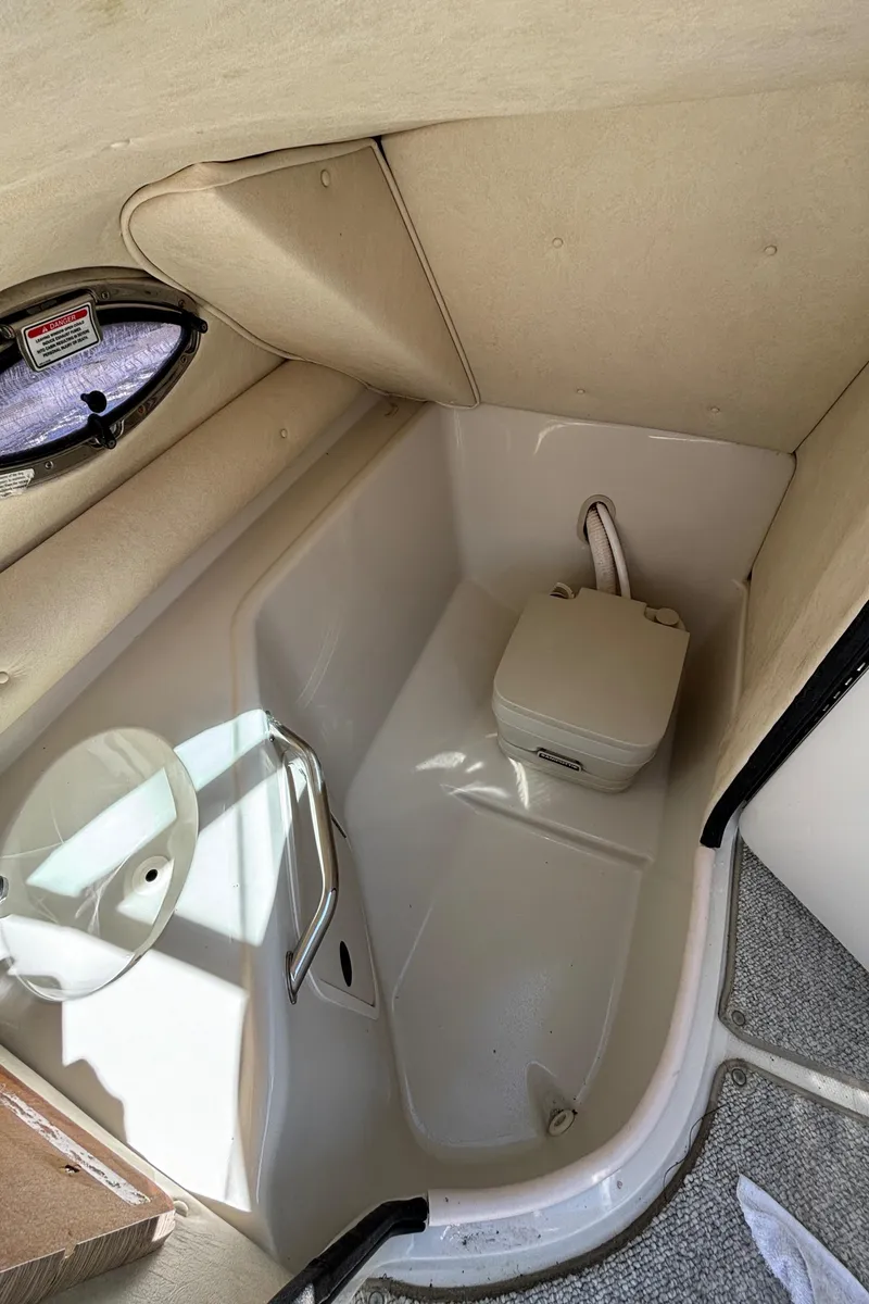 Slide: The Image of 2004 Sea Ray 240 Sundeck interior cabin with portable toilet and porthole window. - 14