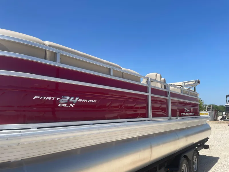 The Image of 2024 Sun Tracker Party Barge 24 DLX pontoon boat with red exterior under clear blue sky. - 0