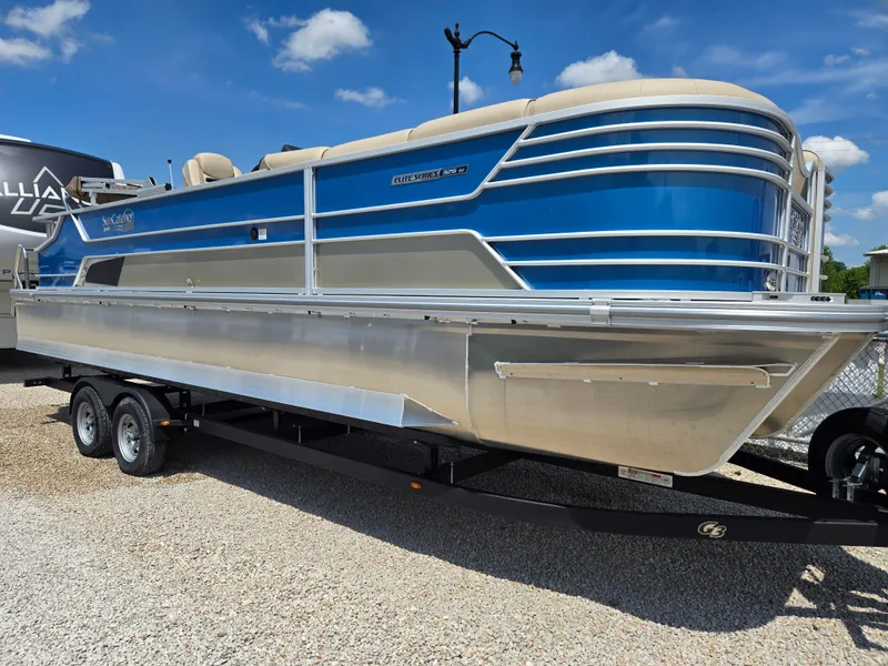 Slide: The Image of 2024 SunCatcher Elite 326 SE pontoon boat, blue and silver, on a trailer under a clear sky. - 2