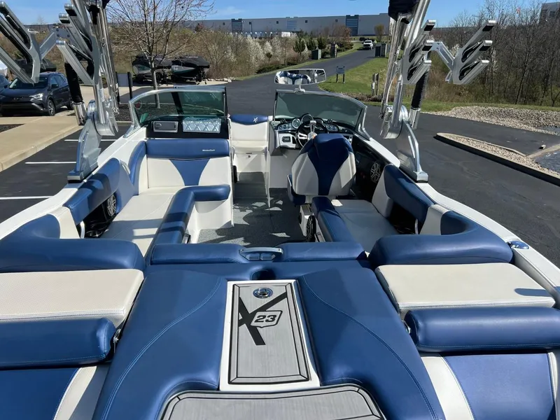 Slide: The Image of 2016 MasterCraft X23 boat interior with blue and white seating, parked on a driveway. - 13