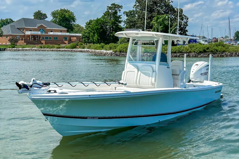 Slide: The Image of 2025 Regulator 26XO boat cruising on a calm waterway near a brick building. - 22