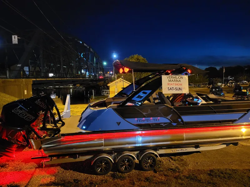 Slide: The Image of 2025 Trifecta 25 Sport RF9 DC 3.0+ boat on trailer at night near marina. - 6