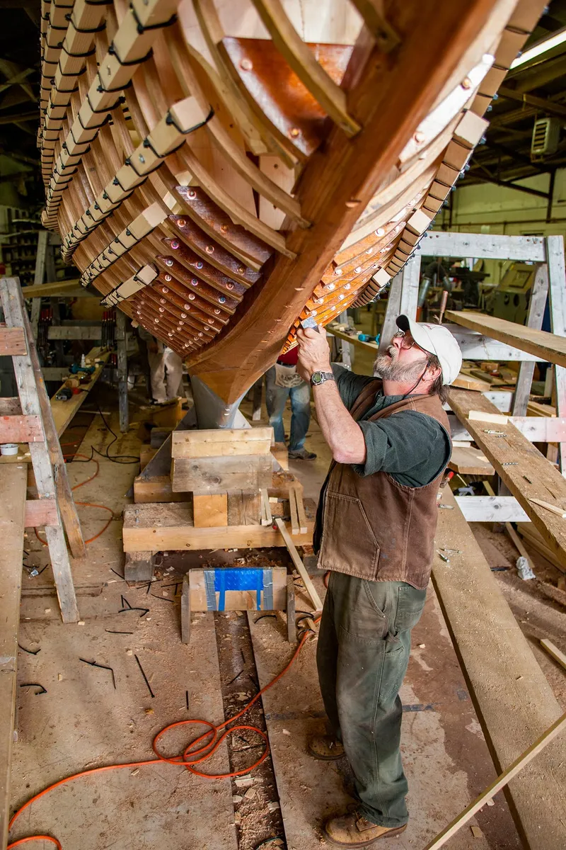 Slide: The Image of Man working on the hull of a 1931 Sparkman & Stephens 36 Sloop in a workshop. - 13