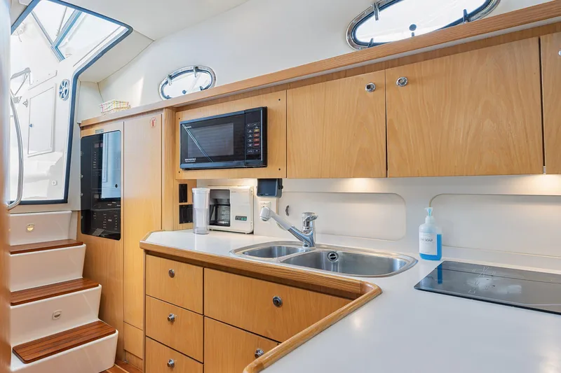 Slide: The Image of 1999 Tiara Yachts 4000 Express kitchen with wooden cabinets, sink, microwave, and stairs. - 4