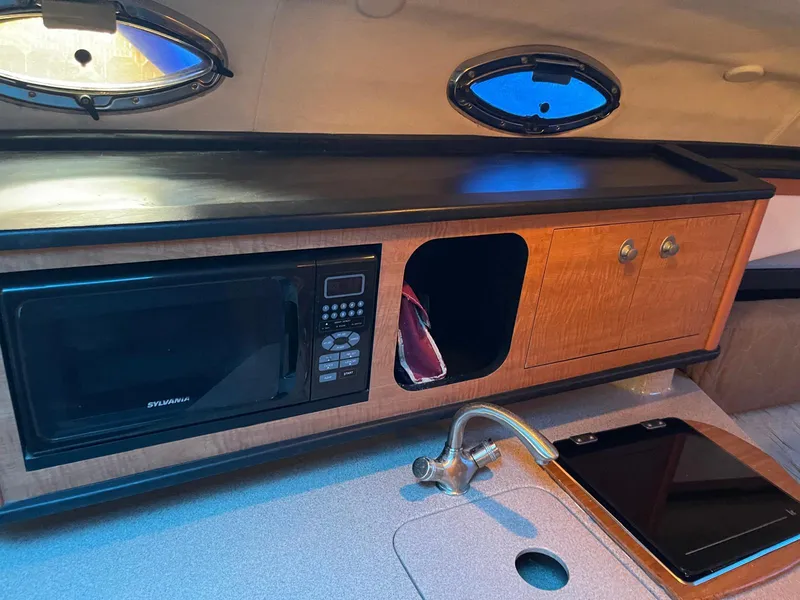 Slide: The Image of 2006 Sea Ray 270 Amberjack interior kitchen with microwave, sink, and storage cabinets. - 11