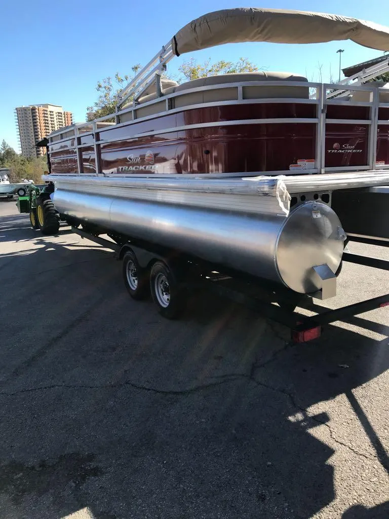 Slide: The Image of 2024 Sun Tracker Party Barge 24 DLX pontoon boat on trailer, parked outdoors. - 2