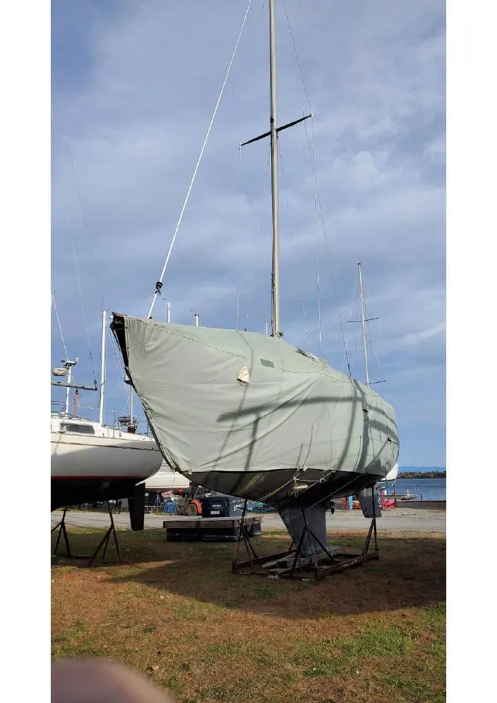Slide: The Image of 1974 Tartan 30 sailboat covered and docked on land under a cloudy sky. - 13