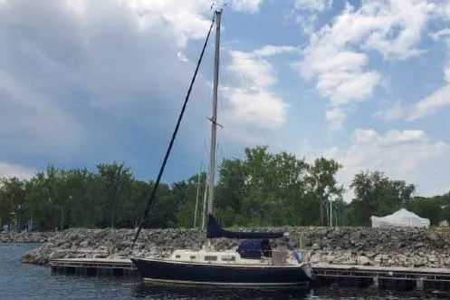 Slide: The Image of 1974 Tartan 30 sailboat docked by rocky shoreline under cloudy sky. - 3