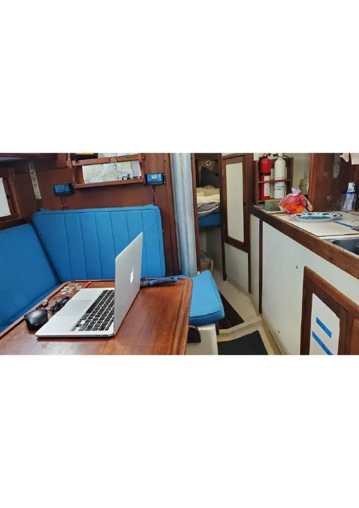 Slide: The Image of 1974 Tartan 30 sailboat interior with blue seating, wooden table, and laptop. - 7