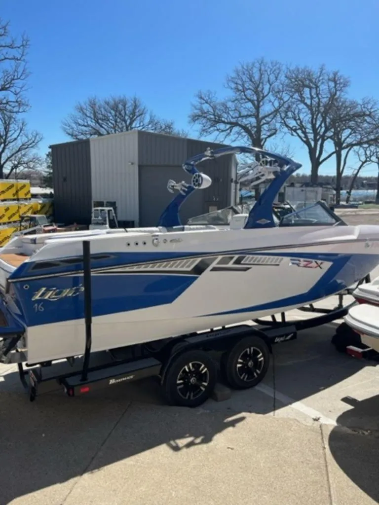 Slide: The Image of 2016 Tigé RZX boat on trailer, blue and white, parked near a building. - 4