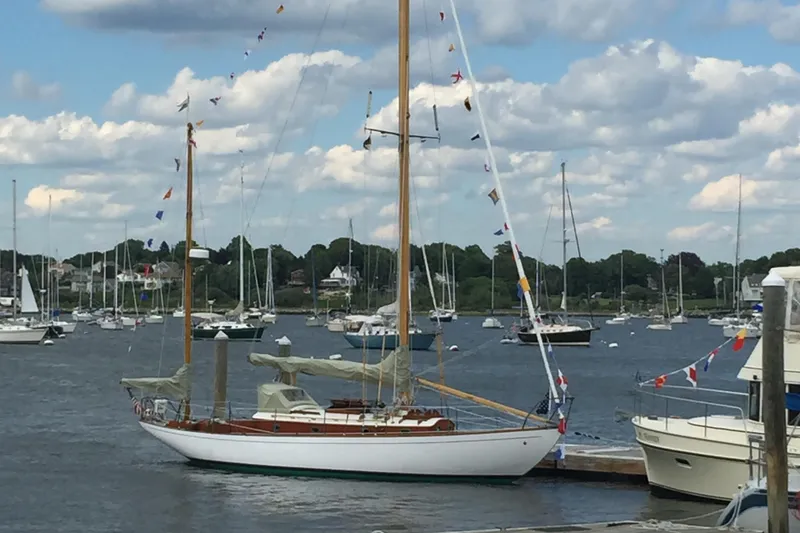 Slide: The Image of 1955 Concordia Yawl sailboat docked in a scenic marina with cloudy sky. - 33