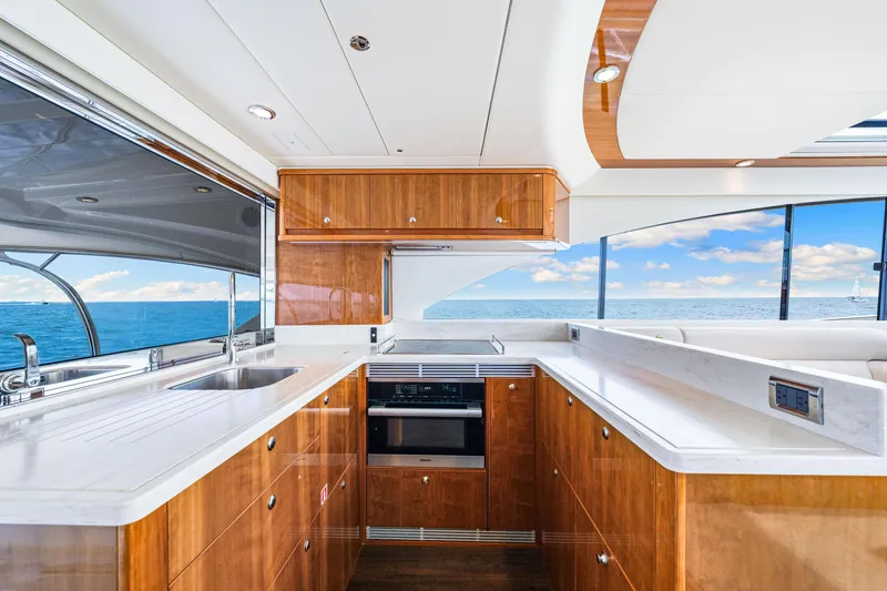 Slide: The Image of 2017 Riviera 575 SUV yacht kitchen with ocean view, modern wooden cabinetry, and white countertops. - 36