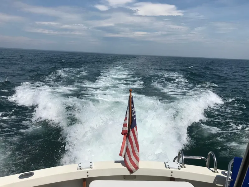Slide: The Image of 1989 Blue Seas Flybridge Cruiser on open sea, American flag waving, leaving a wake. - 40
