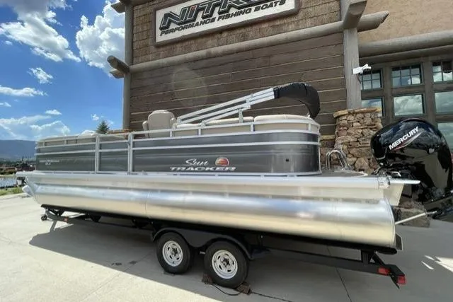 Slide: The Image of 2024 Sun Tracker Party Barge 24 DLX pontoon boat on trailer, parked outside. - 2