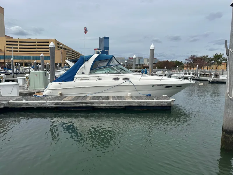 The Image of 2002 Sea Ray 310 Sundancer docked at a marina with cityscape background. - 0