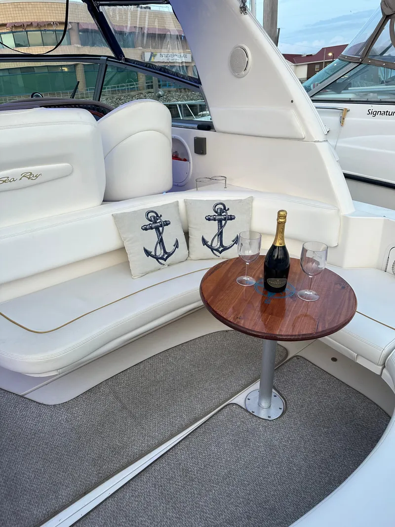 Slide: The Image of 2002 Sea Ray 310 Sundancer interior with anchor pillows, champagne, and glasses on a wooden table. - 13